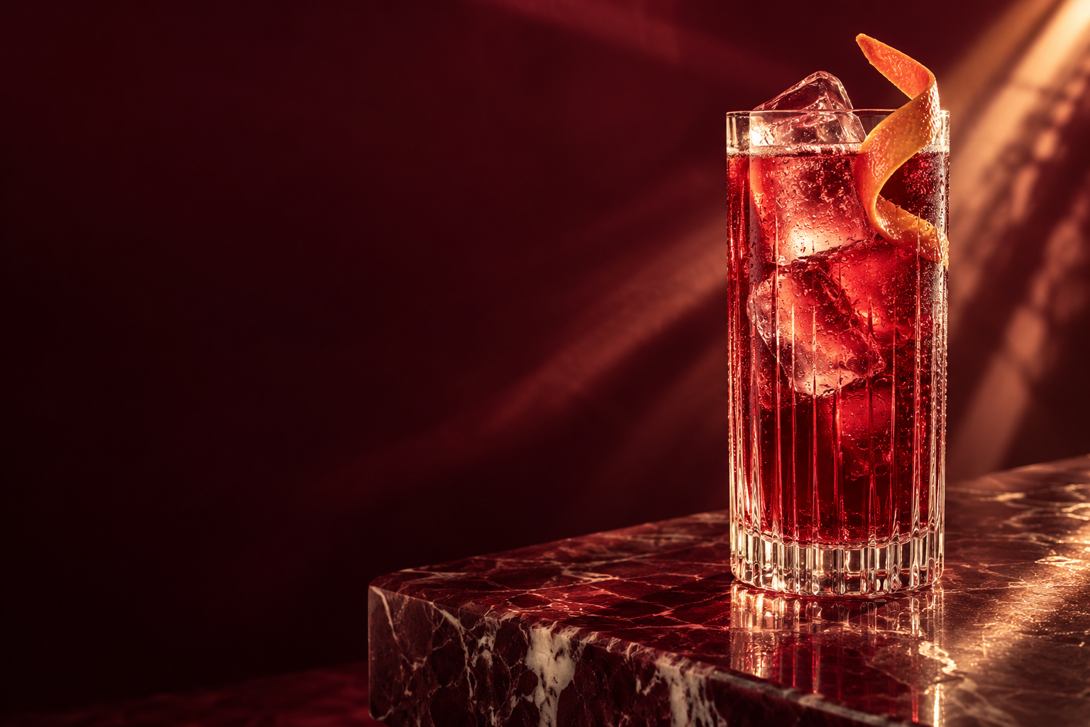 A deep red drink in a crystal highball, with citrus and clear ice